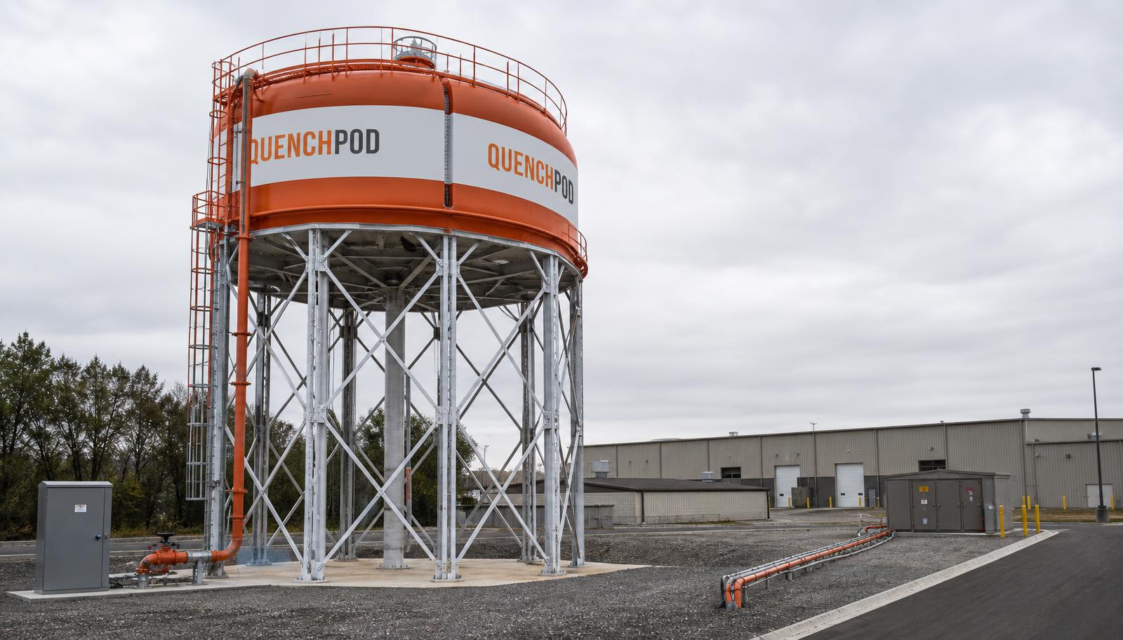 Elevated QuenchPod suppression tower raised on steel legs beside a warehouse, with ground-level control cabinet and distribution pipework